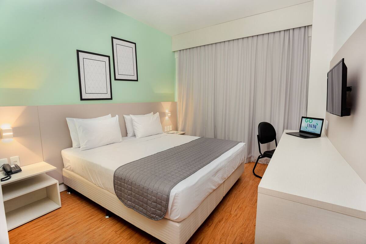 A hotel room with a bed, bedside tables, a desk, a chair, a TV, and curtains.