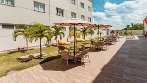 A hotel patio with outdoor seating, a pool, and palm trees. - Hotel Go Inn  Goiana (Goiana)