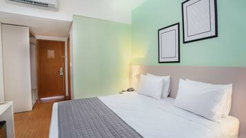 A hotel room with a bed, a bedside table, a lamp, and a wall-mounted air conditioner.