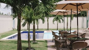 A poolside area with lounge chairs and umbrellas, surrounded by palm trees. - Hotel Go Inn  Goiana (Goiana)