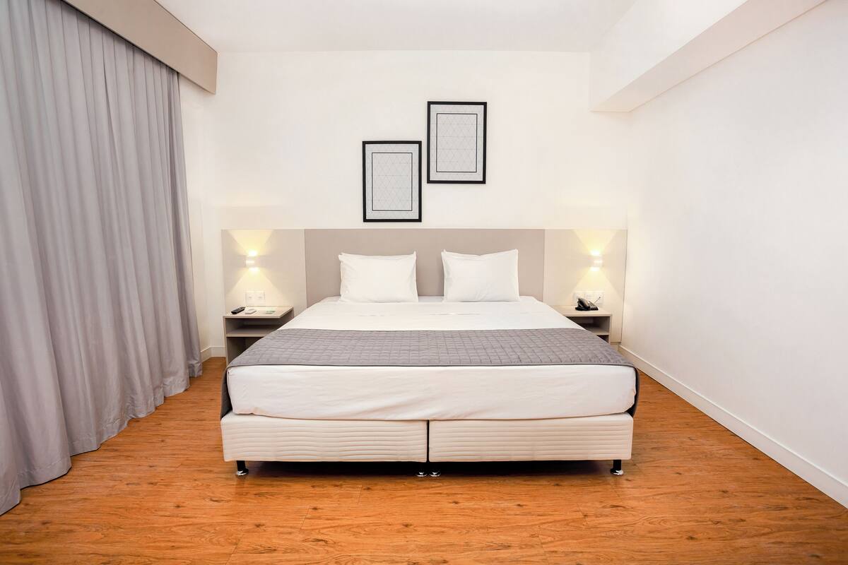 A neatly arranged hotel room with a large bed, two bedside tables, and a headboard.