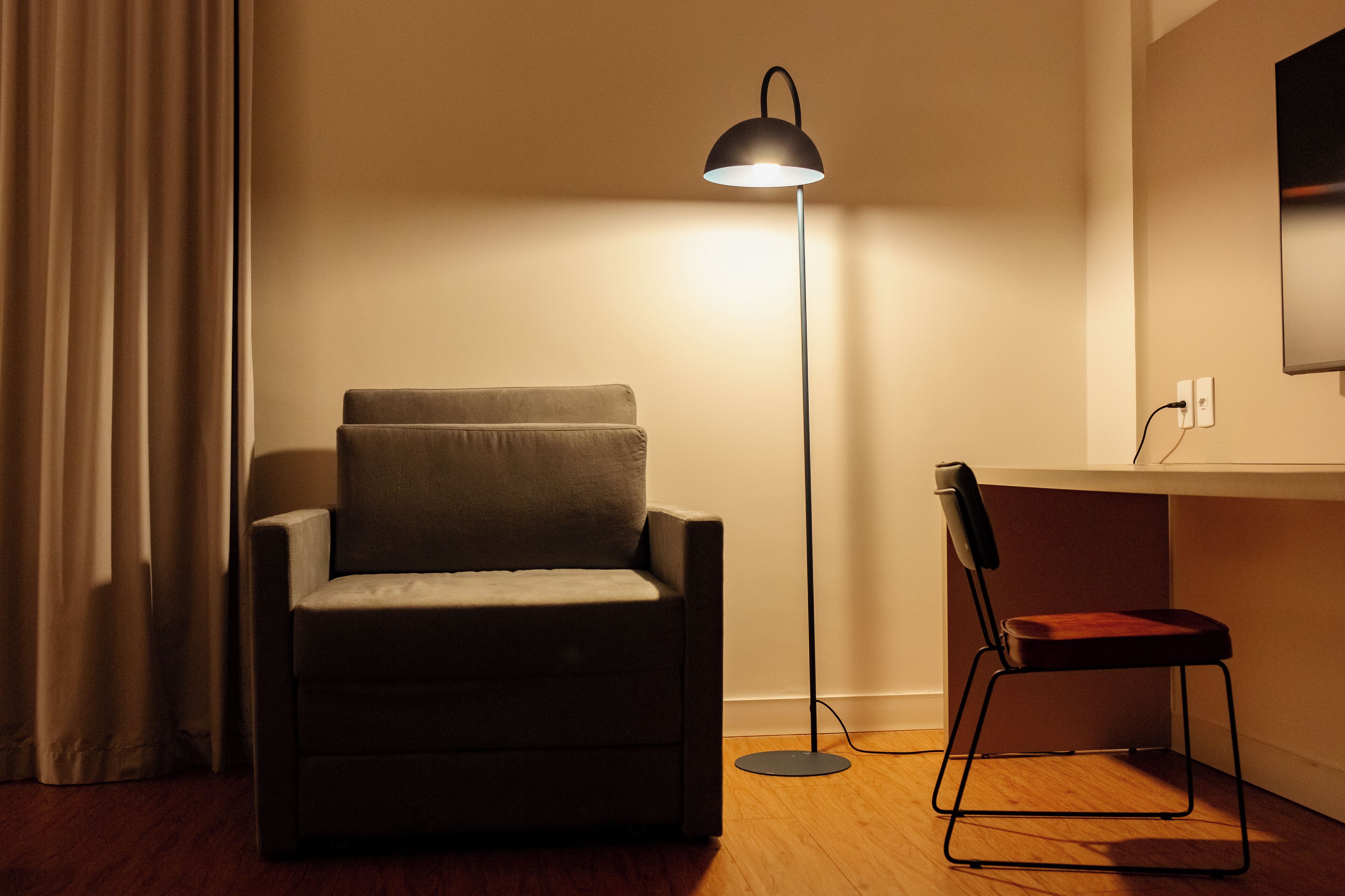 A room with a sofa, a desk with a chair, and a floor lamp.