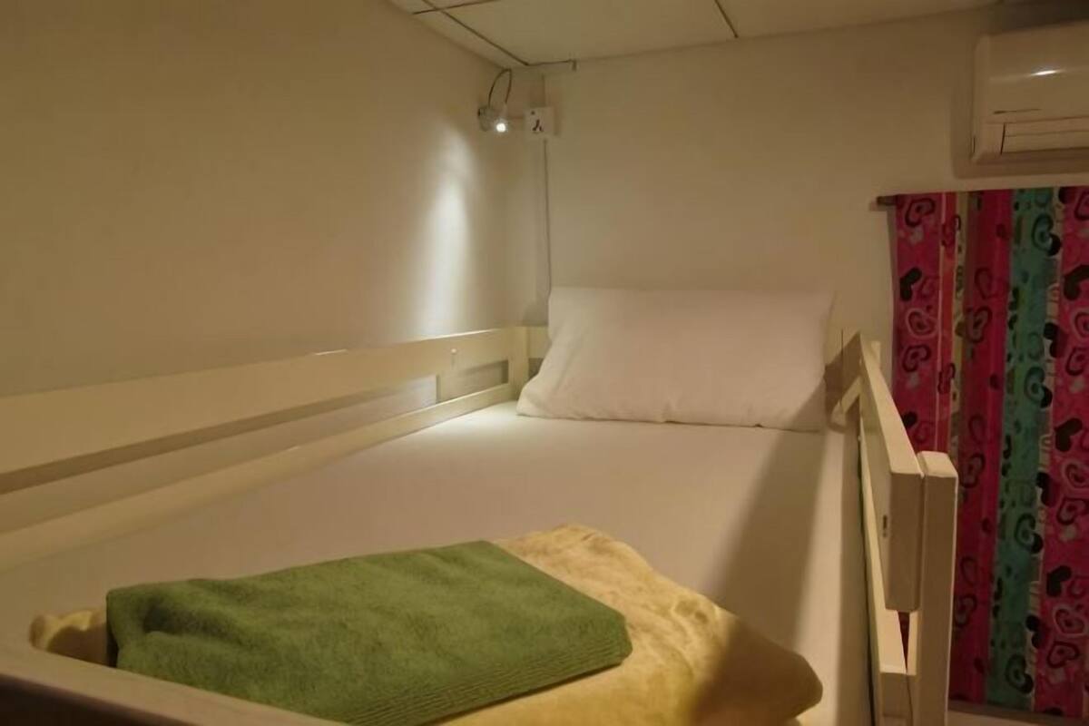 A single bed with a white headboard, a green towel, and a white pillow.