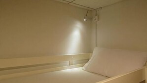 Una cama individual con colchón y almohada blancos, cabecera y lámpara en el techo.