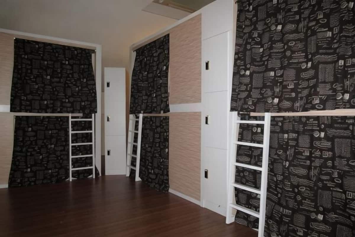 A room with a wooden floor, white walls, and black patterned wallpaper. There are white doors and a white shelf unit.