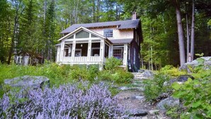 Un chalet rustique entouré d’une forêt dense, doté d’une véranda et de grandes fenêtres.