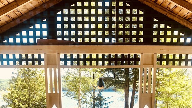 Une terrasse en bois avec une table et des chaises, donnant sur un lac bordé d’arbres et agrémentée d’un belvédère en bois.