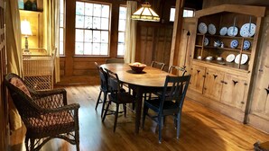 Une salle à manger en bois avec une grande table et des chaises, un luminaire suspendu et un buffet contenant de l’assiette.