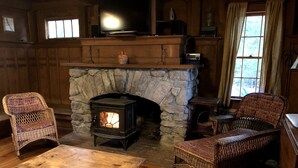 Une pièce chaleureuse avec une cheminée en pierre, des fauteuils en osier, une table en bois et un téléviseur posé sur une étagère en bois au-dessus de la cheminée.