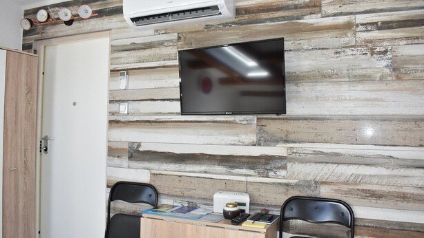 Ett rum med en väggpanel av trä, en platt-TV som är monterad ovanför ett skrivbord, två stolar och en luftkonditioneringsanläggning.