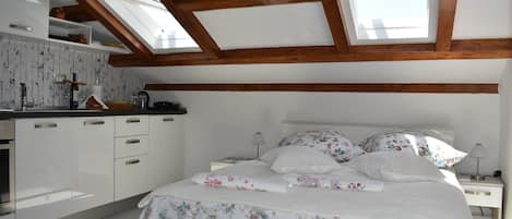 A bedroom with a skylight, a bed with floral bedding, and a white wardrobe.