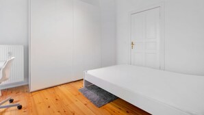 Ein schlicht eingerichteter Raum mit einem weißen Bett, einem weißen Kleiderschrank und einer weißen Heizung.