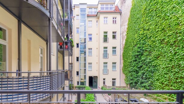 Ein mehrstöckiges Wohngebäude mit Balkonen, einem Holzzaun und einer grünen Hecke.