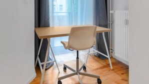 Ein kleiner, moderner Raum mit Schreibtisch und Stuhl aus Holz, einer Heizung und einem Fenster mit Vorhängen.