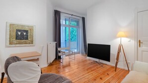 Ein Zimmer mit Holzboden, Schreibtisch, Stuhl, Fernseher und Lampe.