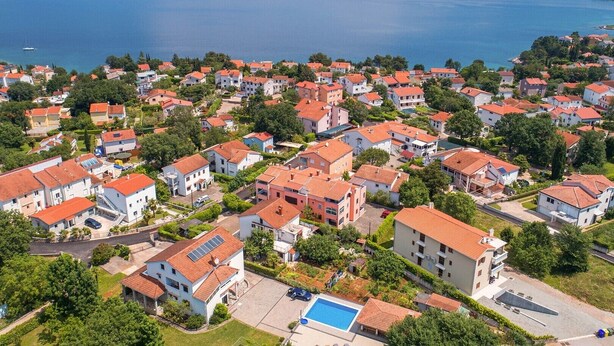 An aerial view of a residential area with houses, a swimming pool, and a body of water in the background.