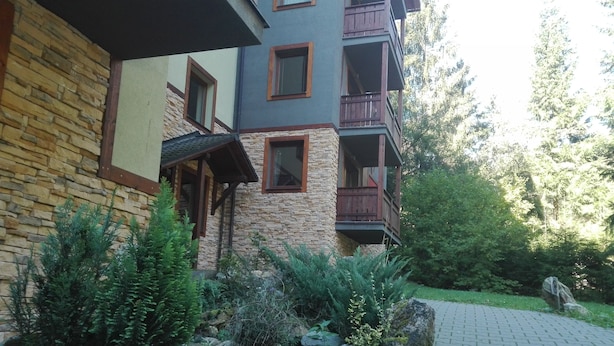 A multi-story building with stone and wood exterior, balconies, and a paved pathway leading to the entrance.