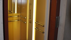 An elevator interior with metallic handrails and a control panel.