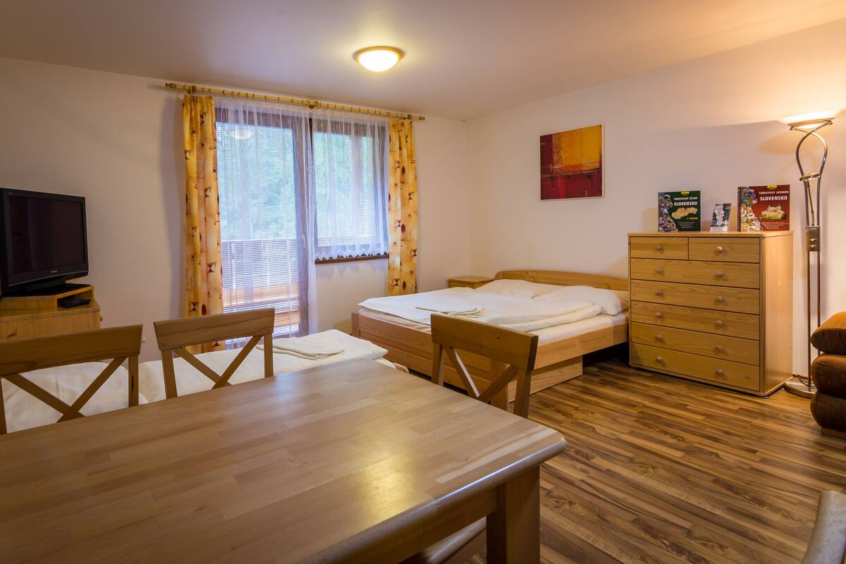 A room with a wooden bed, a wooden table, a TV, and a dresser.