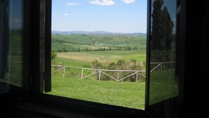 A view through a window with a wooden fence, a grassy field, and distant hills. - STAFFOLINO Apartment 1                                        (siena)