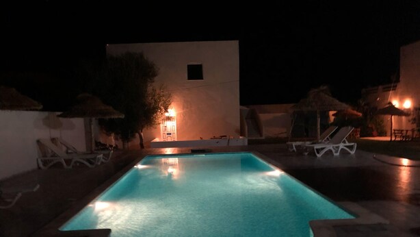 Piscina noturna com superfície de água límpida, cercada por espreguiçadeiras e guarda-sóis.