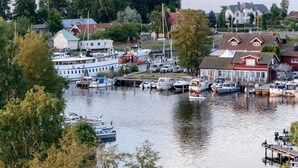 A marina with boats docked, a red building with a white facade, and a large white boat in the background.