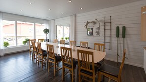 A dining area with a long table and chairs, white walls, and a ceiling with recessed lighting.