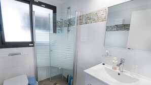 Ein modernes Badezimmer mit einer Duschkabine aus Glas, einem weißen Waschbecken inklusive Spiegel und einer Toilette.