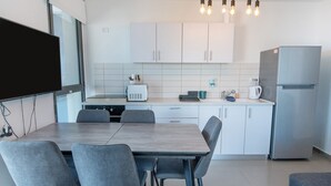 Eine moderne Küche mit weißen Schränken, einem Edelstahl-Kühlschrank, einem Esstisch mit vier Stühlen und einem eingebauten Backofen.