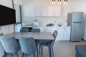 Una cocina moderna con armarios blancos, un refrigerador de acero inoxidable, una mesa de comedor con cuatro sillas y un horno empotrado.