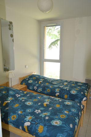 A room with two beds, a mirror, a window, and a lamp.