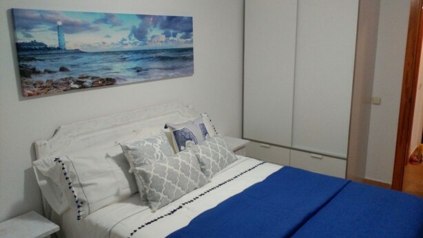 A bedroom with a bed, a nightstand, a wardrobe, and a painting of a lighthouse on the wall. - RELAX AND TRAQUILADAD pair all kinds of families with or without children  (corralejo)