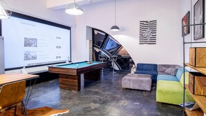 A modern living room with a pool table, comfortable seating, a large screen displaying property listings, and a staircase leading to an upper level. - Dream Aparts - Lofty Scheiblera (Lodz)