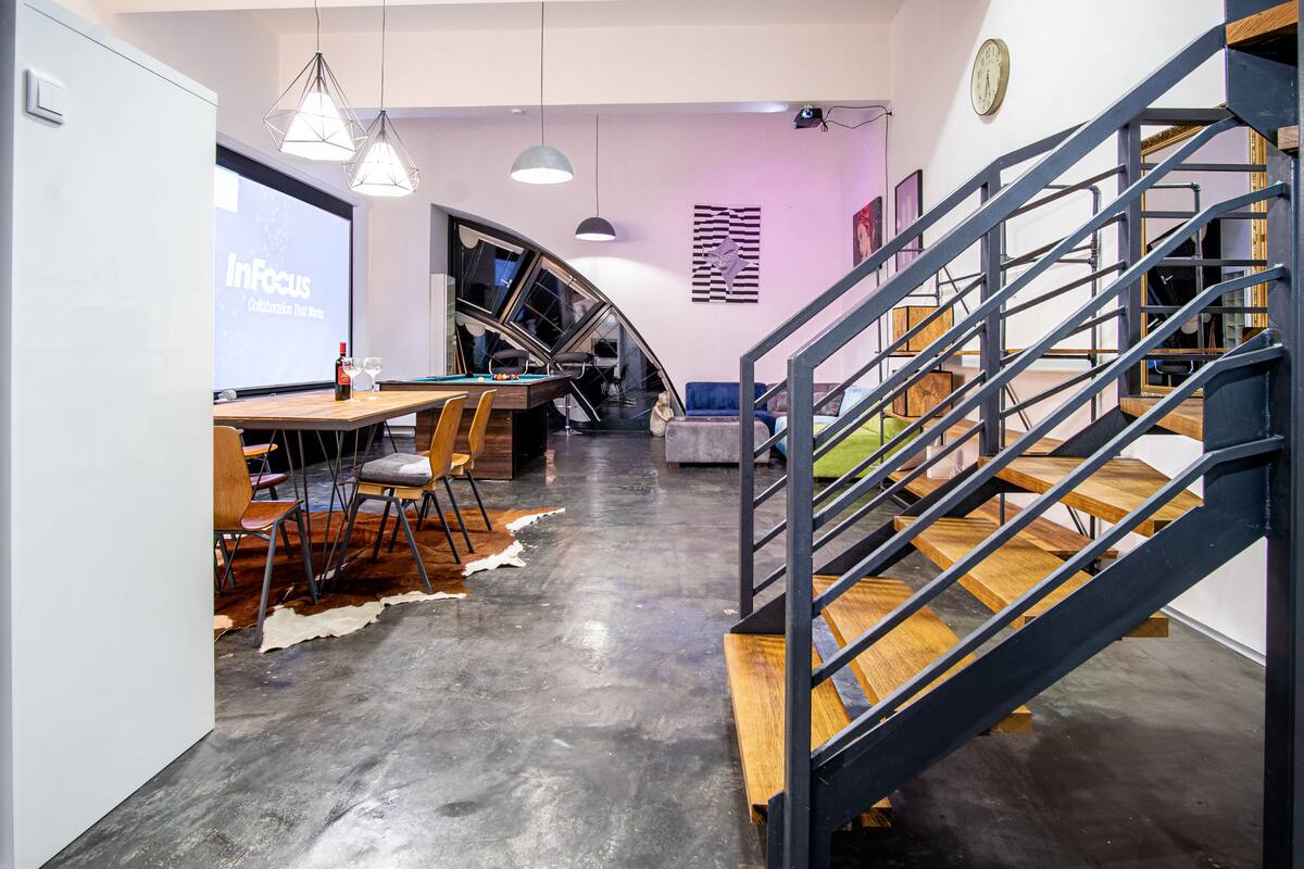 A modern office space with a wooden desk, chairs, a large screen displaying 'InFocus Collaboration That Moves', and a staircase with metal railings.