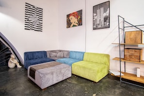 Een moderne woonkamer met een hoekbank, een klein voetenbankje en een metalen wandrek.