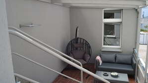 Un balcón con un sofá gris, una silla de mimbre y una mesita con un cuenco y una taza.