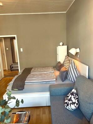 Un dormitorio moderno con una cama, un sofá gris, una lámpara de noche y un reloj de pared.