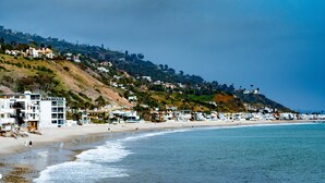 A beach with a building on the left and a hill in the background. - Oceanfront on Dry Sandy Carbon Beach - Sandpiper (Malibu)