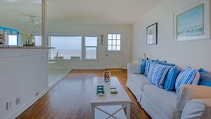 A spacious living area with a white couch, a coffee table, and a view through a glass door to the outside. - Oceanfront on Dry Sandy Carbon Beach - Sandpiper (Malibu)