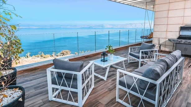 Un patio moderno al aire libre con mobiliario blanco, una parrilla y vistas al mar.