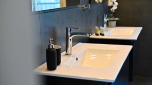 Un baño moderno con dos lavamanos blancos, un grifo cromado y un dispensador de jabón negro.