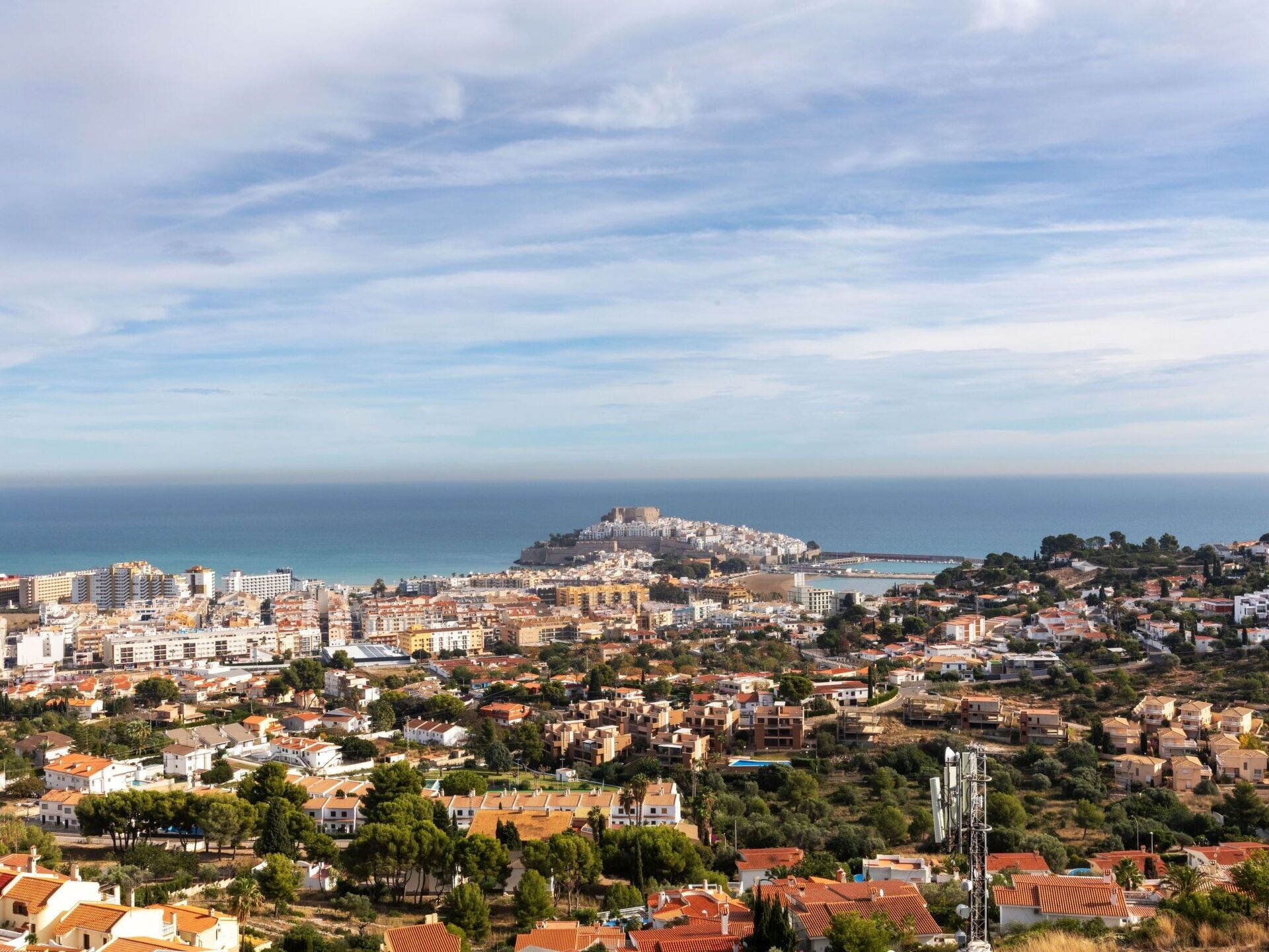 Un paysage urbain côtier avec une imposante forteresse perchée sur une colline, des quartiers résidentiels densément peuplés et une vue dégagée sur la mer.