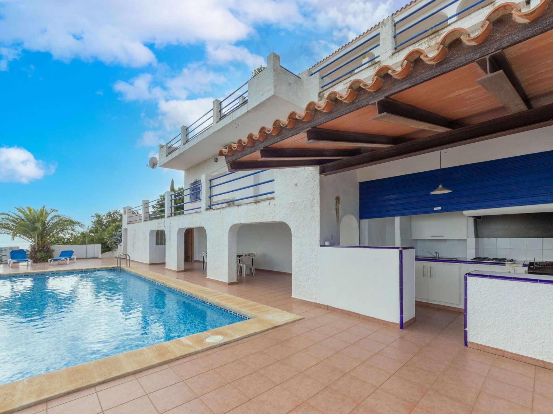 A poolside area with a swimming pool, outdoor seating, and a kitchen area with a blue countertop.