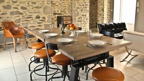 Comedor con pared de piedra, mesa de madera dispuesta para seis personas y sillas de cuero.