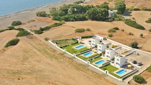 A coastal hotel with multiple swimming pools, a road, and surrounding hills. - White House Villas (Rhodes)