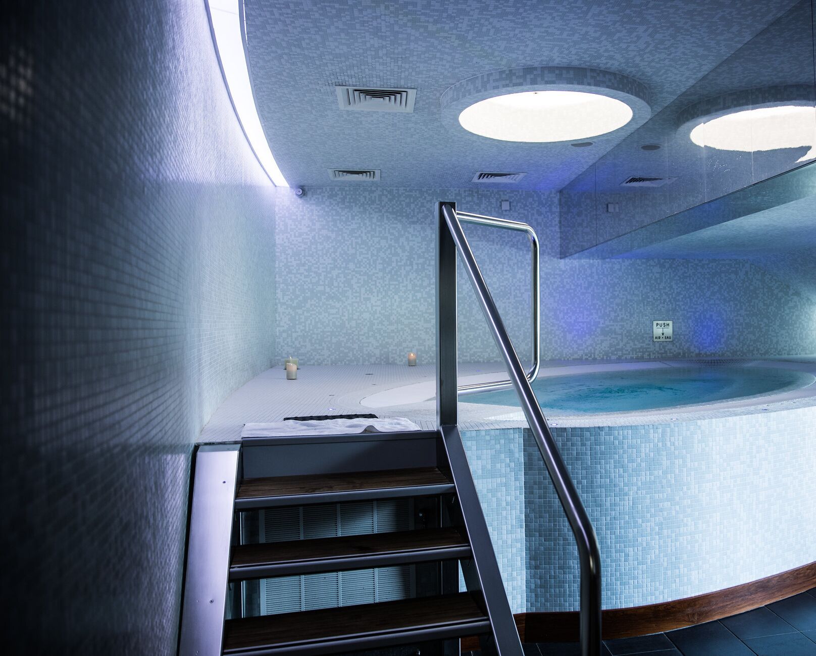 Ein moderner, überdachter Schwimmbereich mit Glasabdeckung, einer Holztreppe und einer Decke mit Einbauten.
