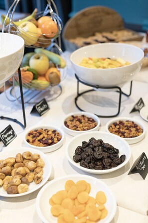 Taula de buffet amb diferents aliments, incloent fruita, fruits secs i pastisseria seca.