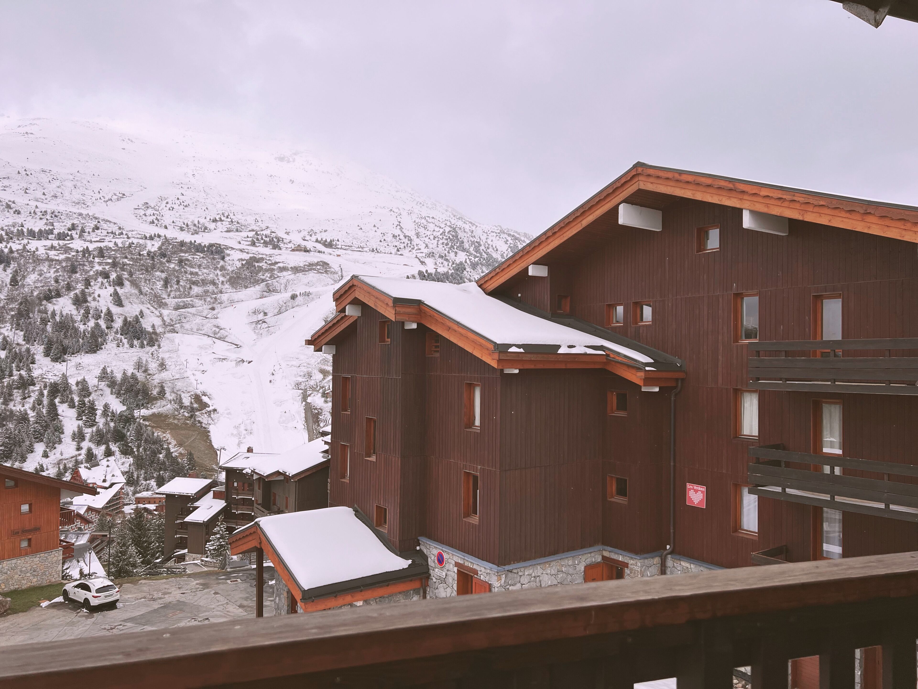 A wooden building with multiple windows and a snow-covered roof, surrounded by a mountainous landscape.