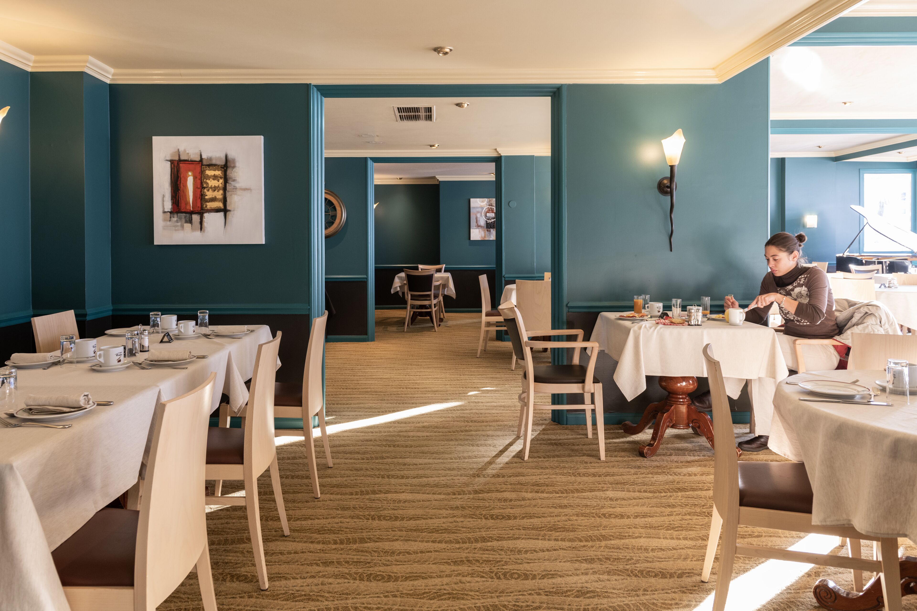 Un restaurante con varias mesas y sillas, una persona cenando, y obras de arte en las paredes.