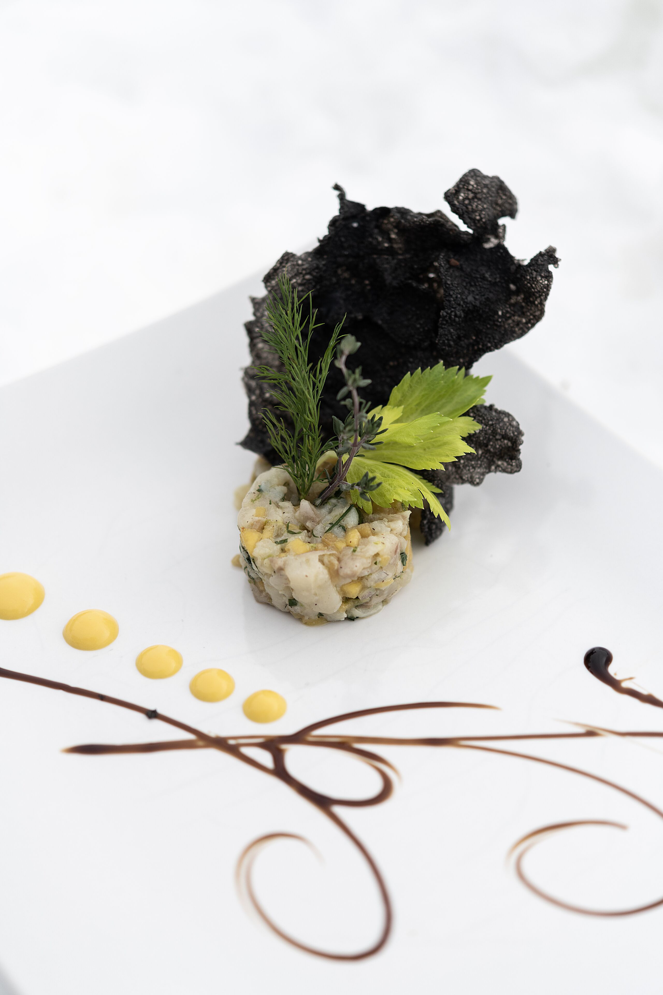Plat amb un centre esfèric, adornat amb herbes verdes, damunt d'un plat blanc amb punts grocs i remolins marrons.